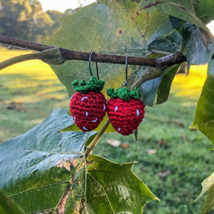 Two strawberry earrings made of crocheted embroidery floss are hanging from a small sweetgum branch.