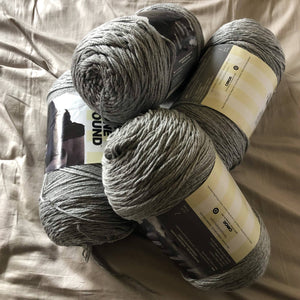 There are four skeins of gray yarn on a neutral background to show a color option for the custom ankle duster cardigan. 