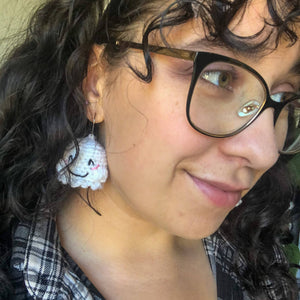 A woman with curly brown hair and glasses faces to the side of the camera with one ghost earring visible. 