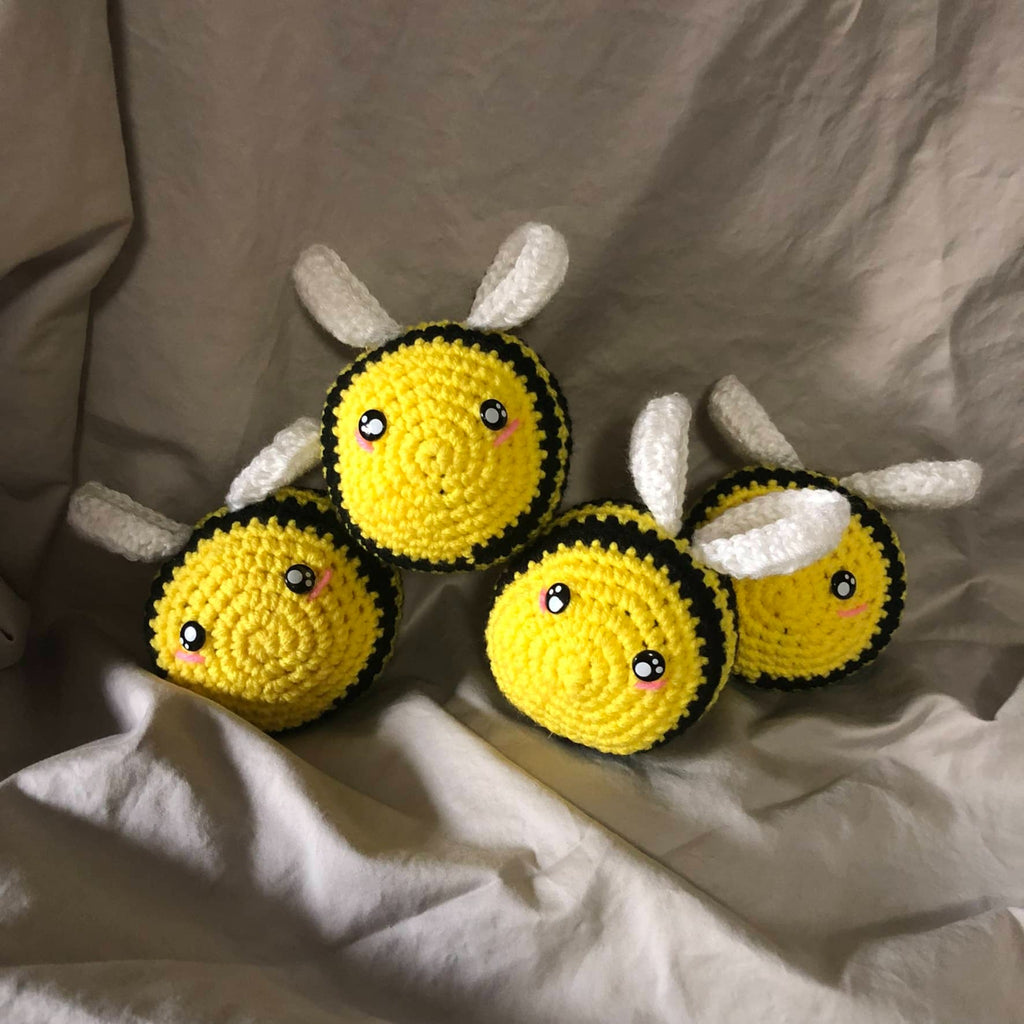 Four crocheted and stuffed bees in yellow and black with white wings. They have safety eyes and little blush spots on their faces. 