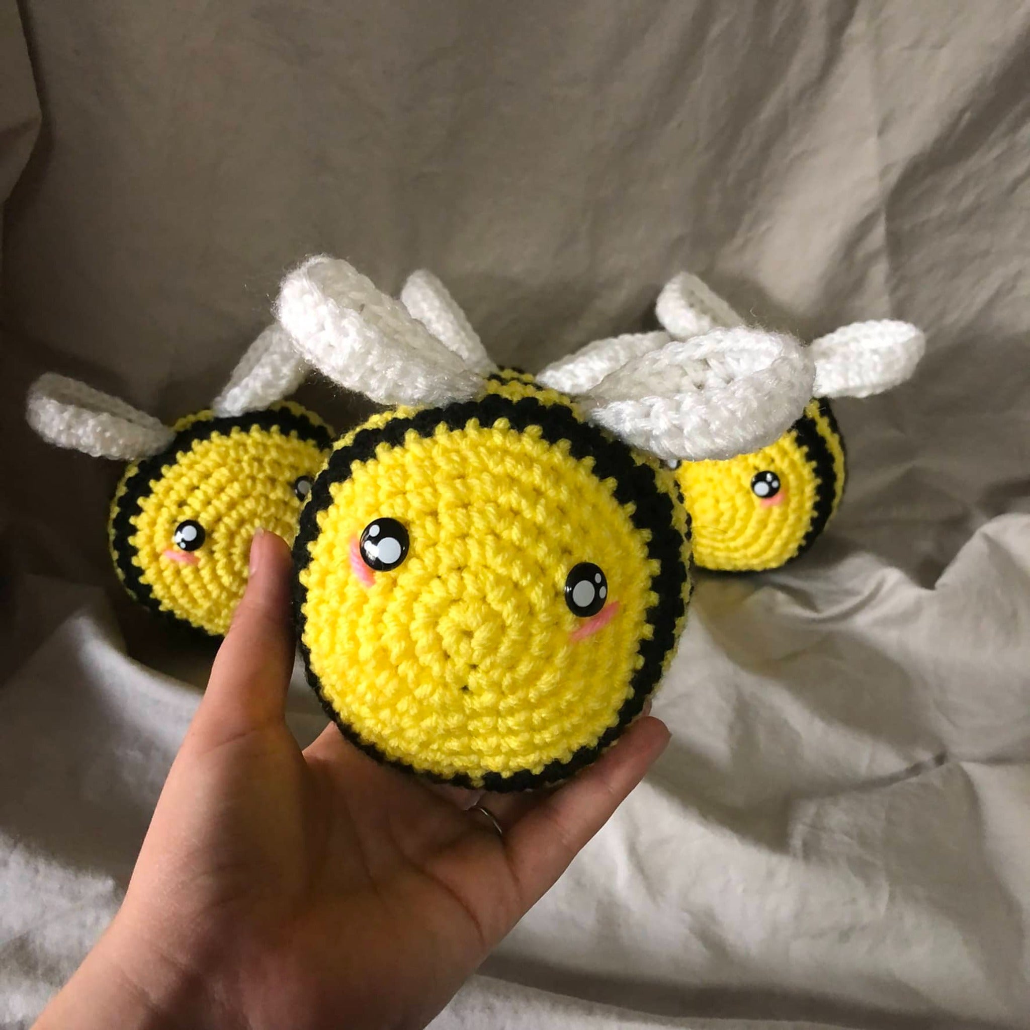 Four crocheted and stuffed bees in yellow and black with white wings. One is being held up closer to the camera while the other three are behind him.