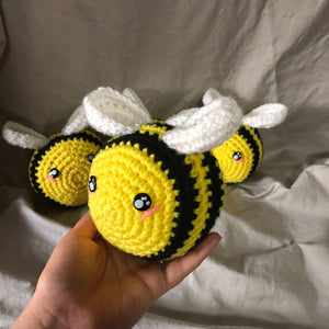 Four crocheted and stuffed bees in yellow and black with white wings. One is being held up closer to the camera while the other three are behind him.