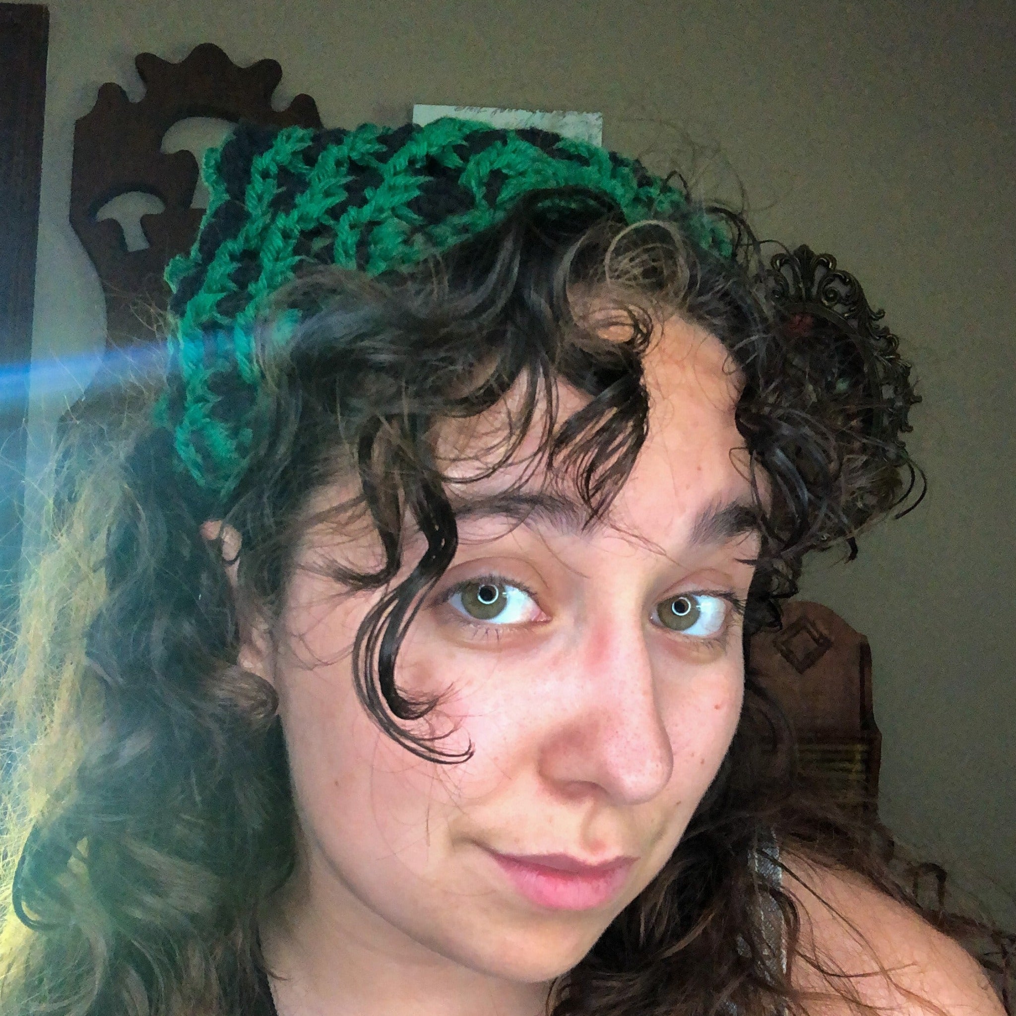 A woman with brown curly hair looks into the camera wearing a green and black head scarf bandana. 