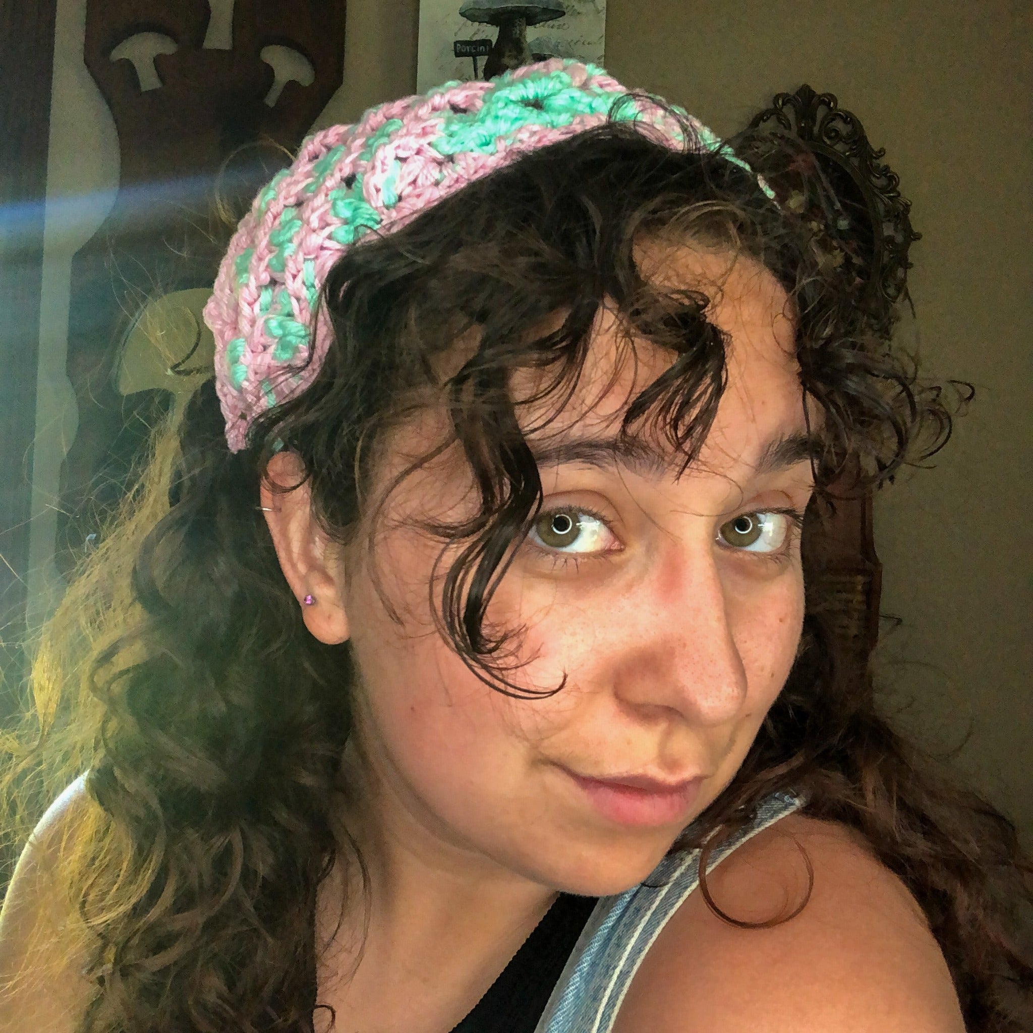 A woman with brown curly hair looks into the camera wearing a mint green and pink head scarf bandana.