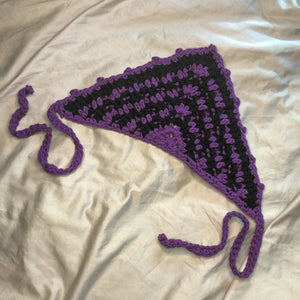 A purple and black striped head scarf bandana lays on a neutral background.