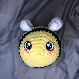 A giant plushie bee made of chenille yarn with big felt eyes is on a neutral background, facing the camera.