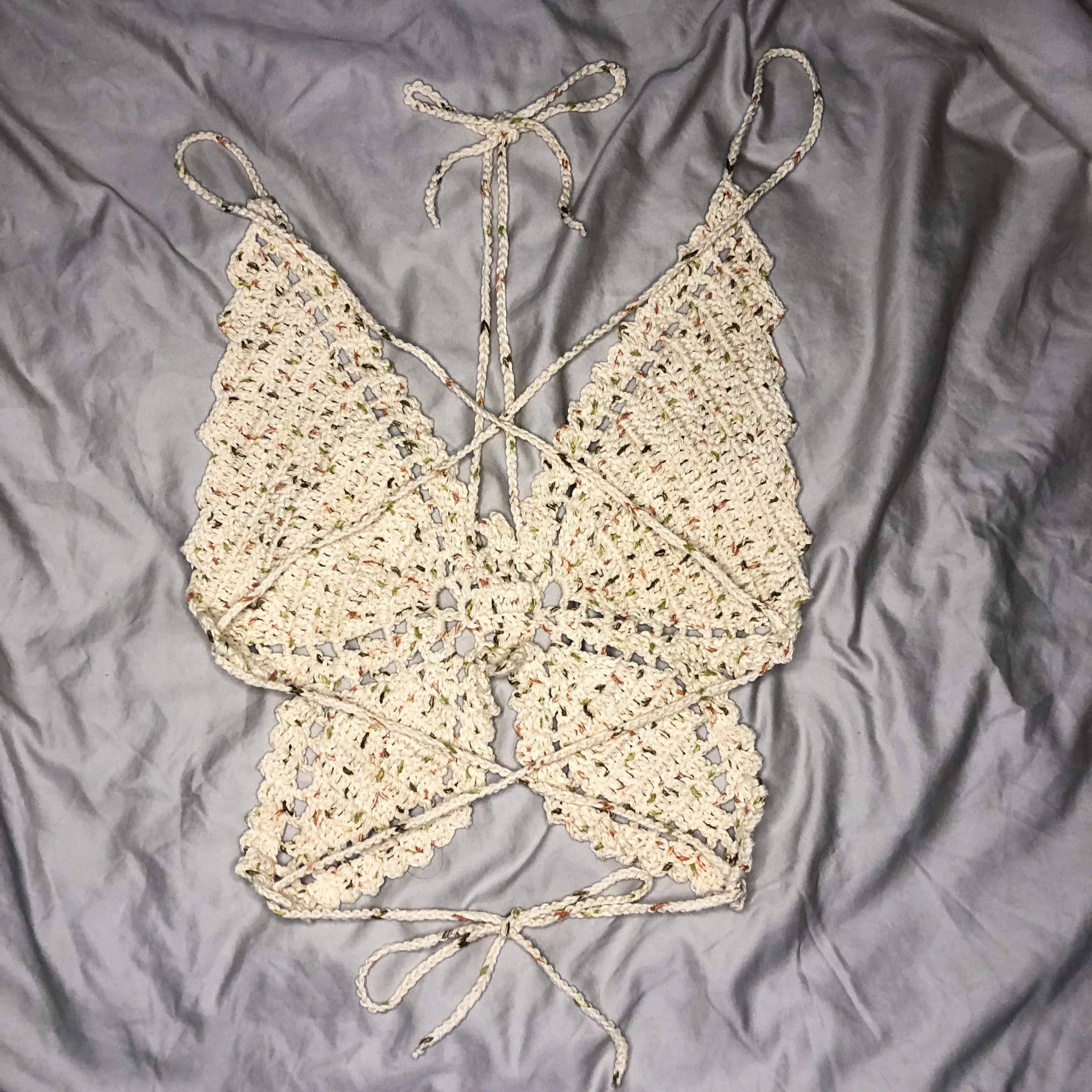 An extra small butterfly top is laying on a neutral background, facing away from the camera to show off the crisscross straps. 