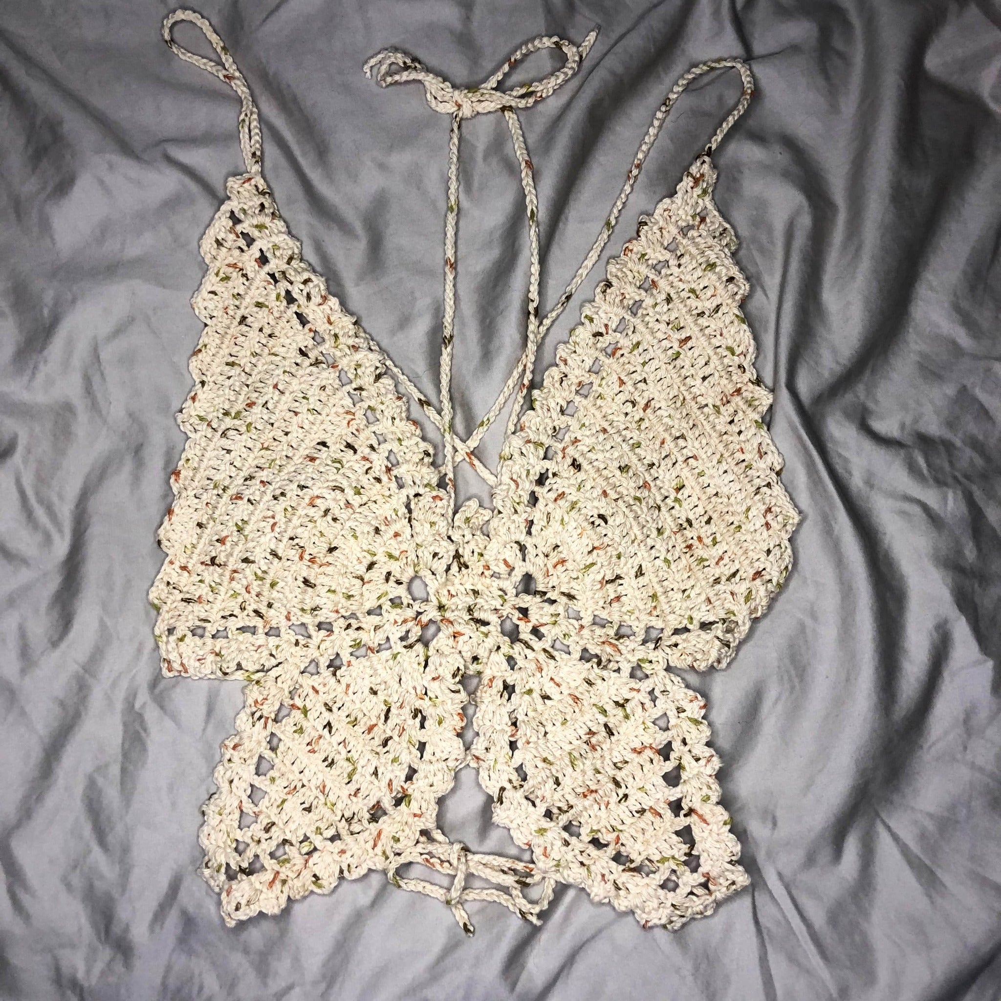 A crochet butterfly top is laid out on a neutral background, showing the entire top in a flat lay position.