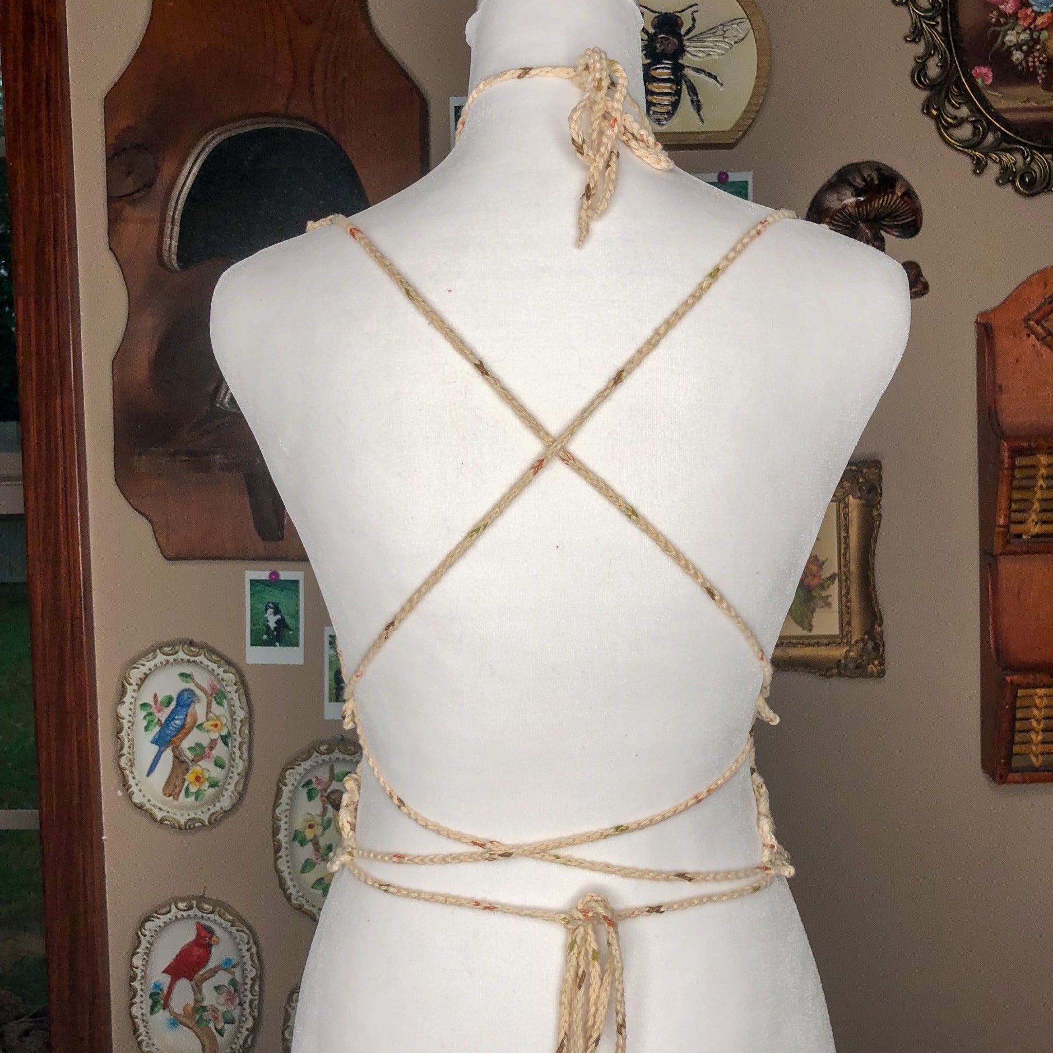 An extra small butterfly top is on a mannequin facing away from the camera to show off the crisscross straps. In the background are multiple wall decorations including a mushroom mirror and porcelain birds. 