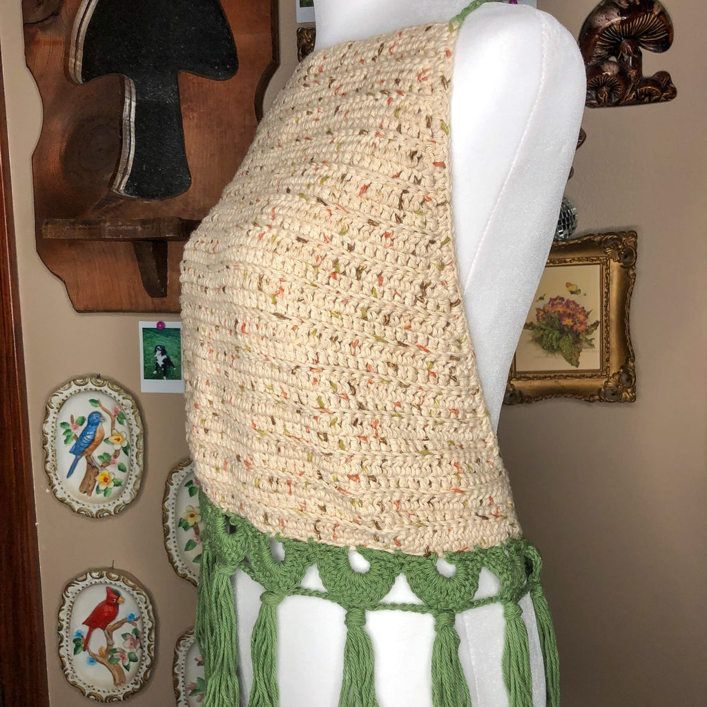 A sage top is on a mannequin, facing slightly off center to show the top at an angle on the mannequin. In the background are trinkets including a mushroom mirror, some framed drawings, and some porcelain wall hangings.