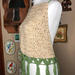 A sage top is on a mannequin, facing slightly off center to show the top at an angle on the mannequin. In the background are trinkets including a mushroom mirror, some framed drawings, and some porcelain wall hangings.