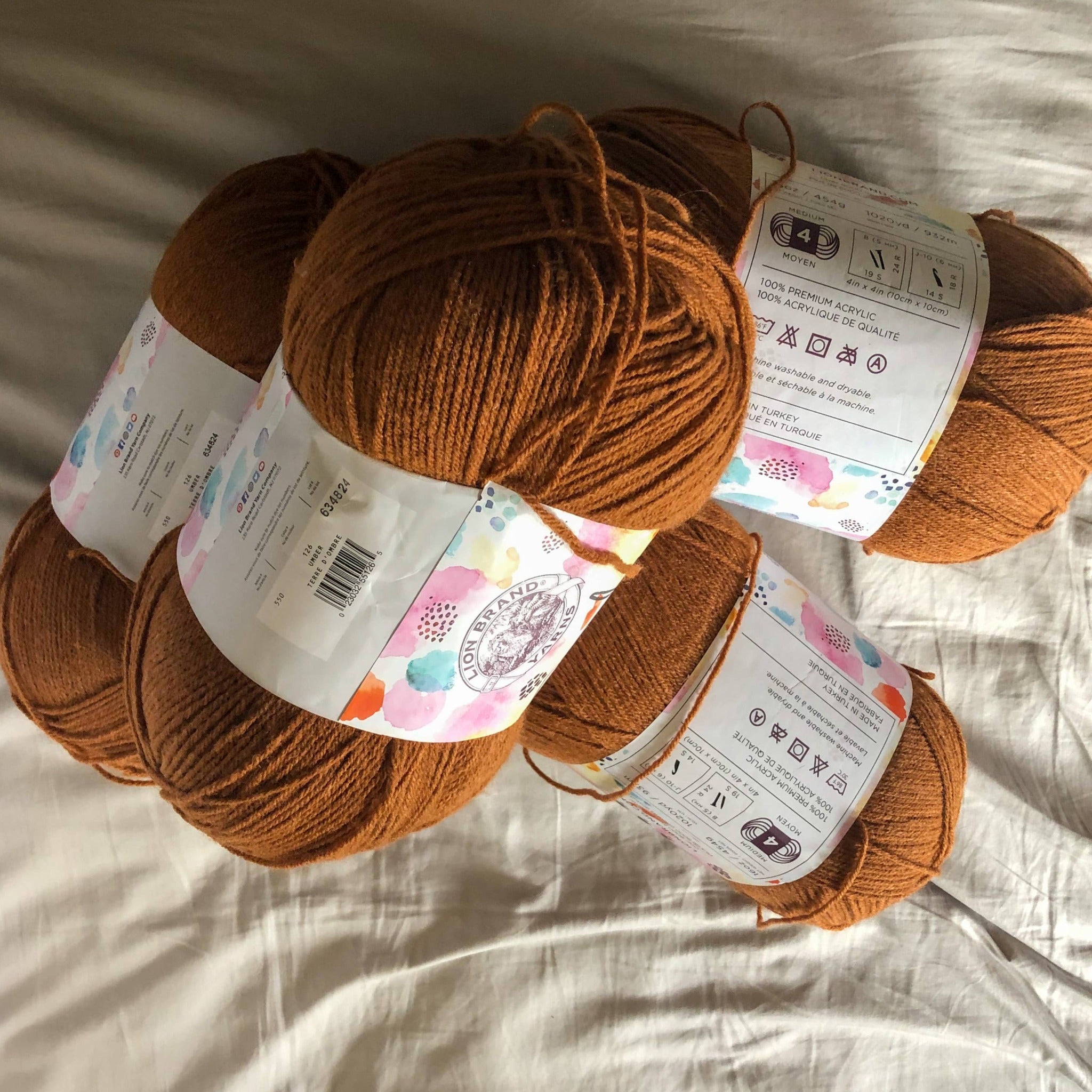 There are four skeins of pumpkin spice orange yarn on a neutral background, showing one of the color options for the custom ankle duster cardigan. 