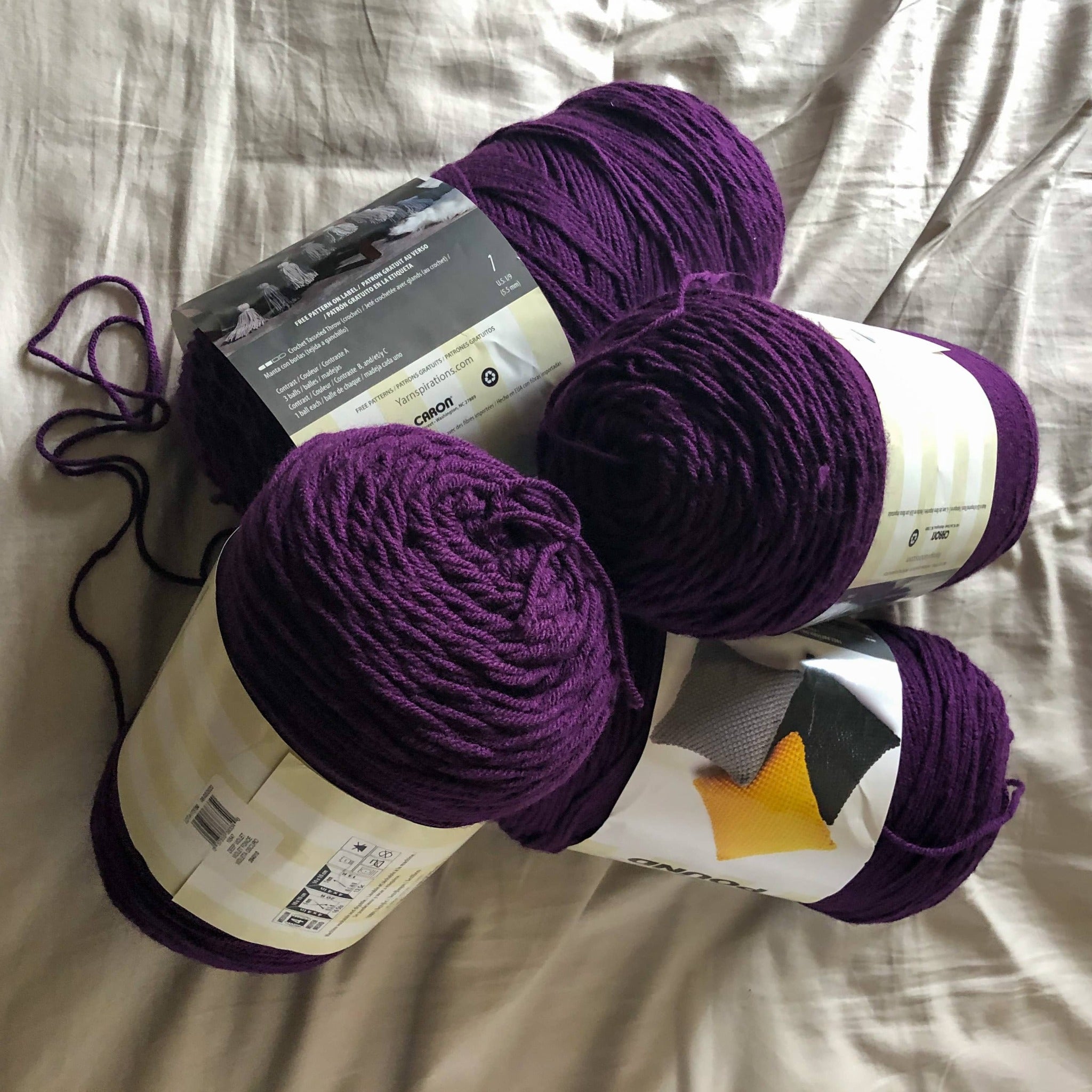 There are four skeins of purple yarn laying on a neutral background to show one of the color options for a custom ankle duster cardigan. 